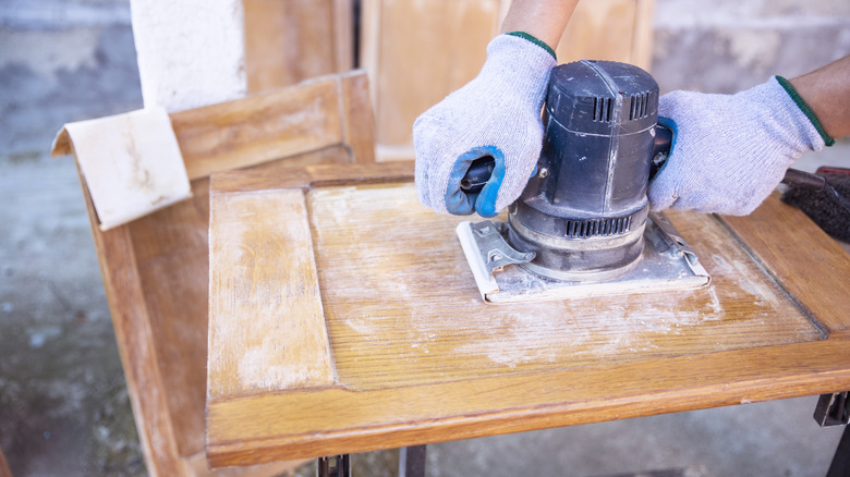 A person sanding the front of a cabinet