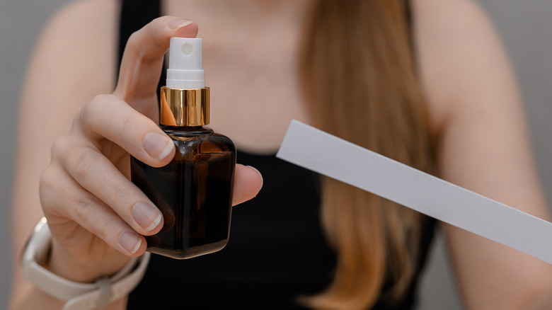 A person's hand holding a spray bottle and a cardboard strip