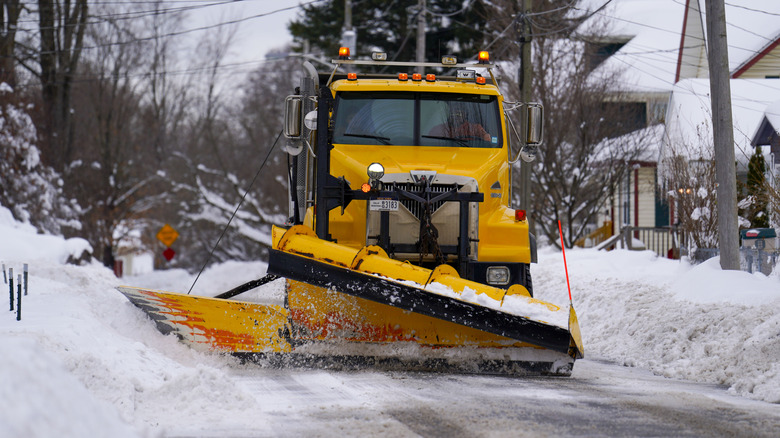 Snow plow pushing snow toward homes along a residential street.