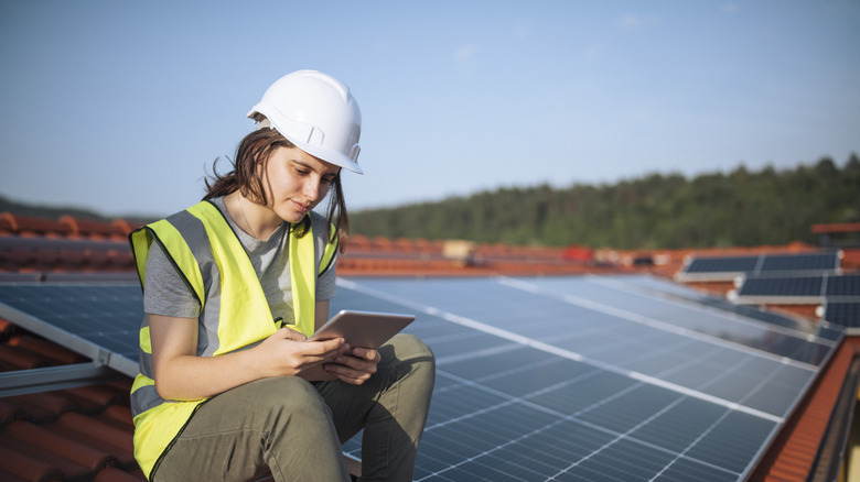 Solar engineer checking tablet on a rooftop with solar panels in the background.