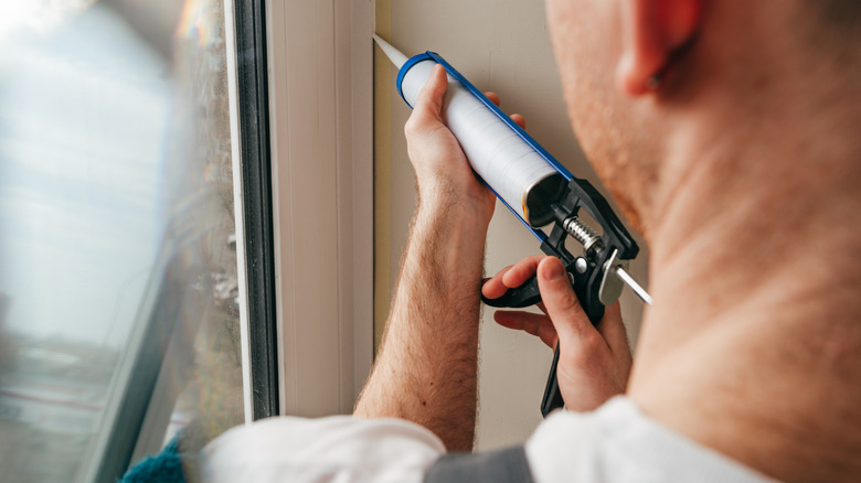 a man caulking a gap near a window
