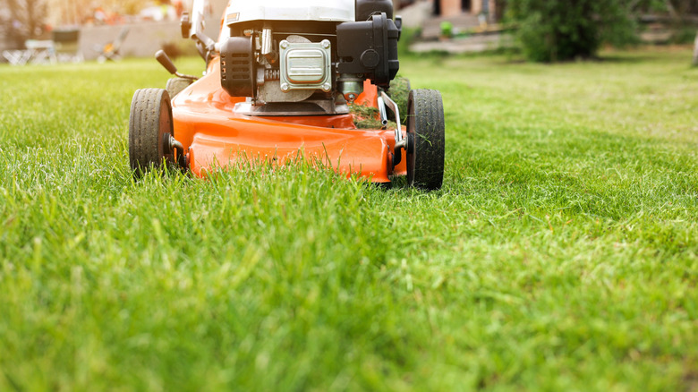 A closeup of an orange lawn mower mowing grass in a backyard with outdoor furniture in the background