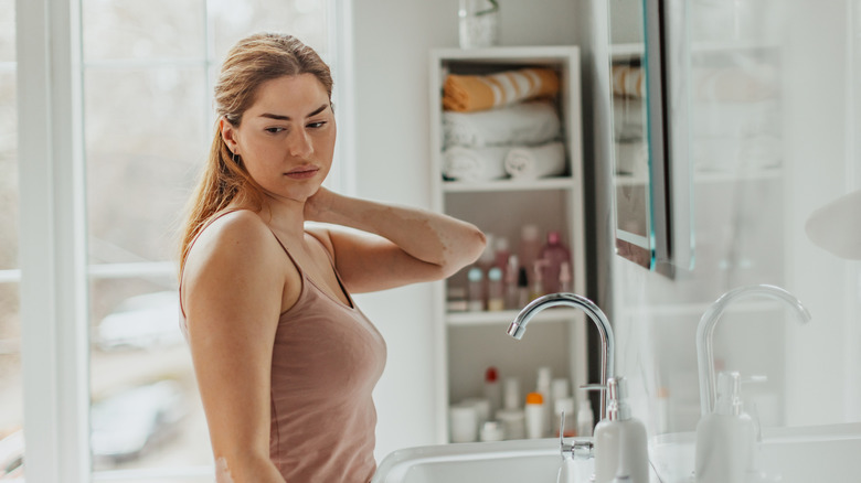 A woman stands by open shelving while thinking in a bathroom