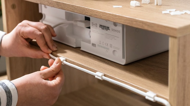 Person attaching TRIXIG 150-piece Cable Management Set to back of shelves