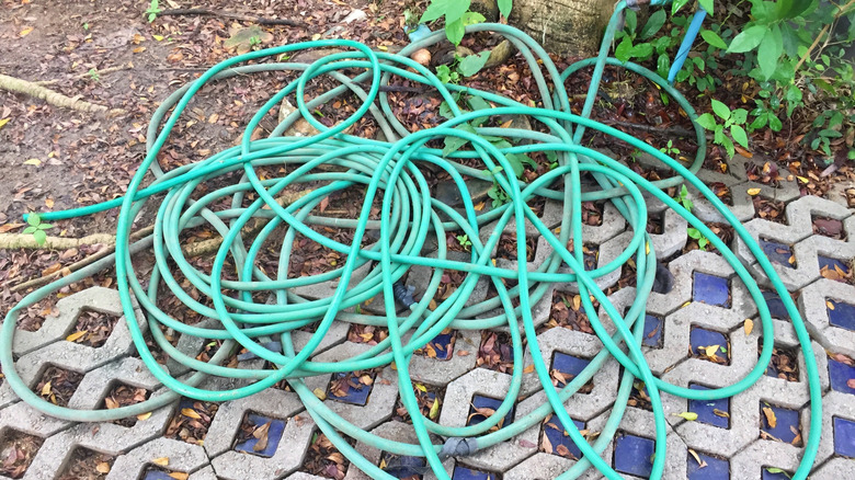 a tangled green garden hose creating clutter on outdoor pavers