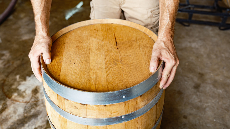 Hands holding a wooden whisky or wine barrel with metal rings