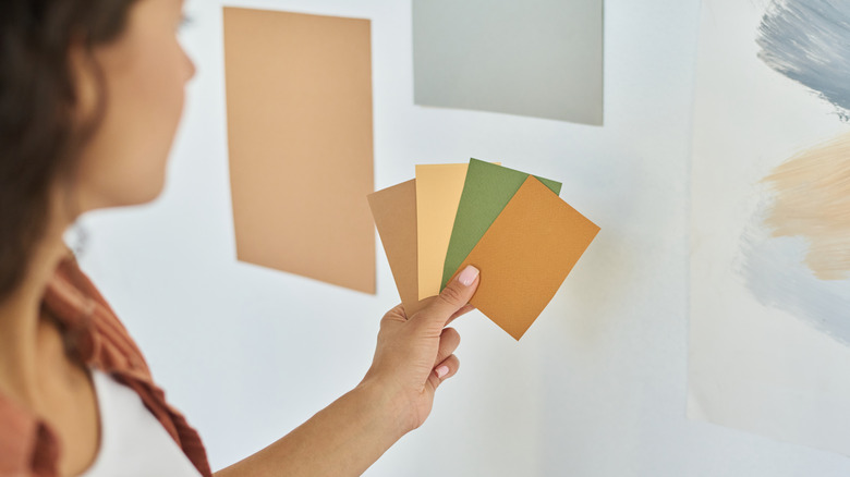 a woman holds paint samples by an unpainted wall