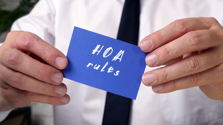 A man's hands hold a small blue card that says "HOA Rules".