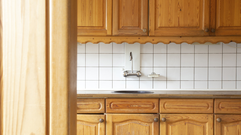Close-up of dated brown wood kitchen cabinets with old scalloped trim