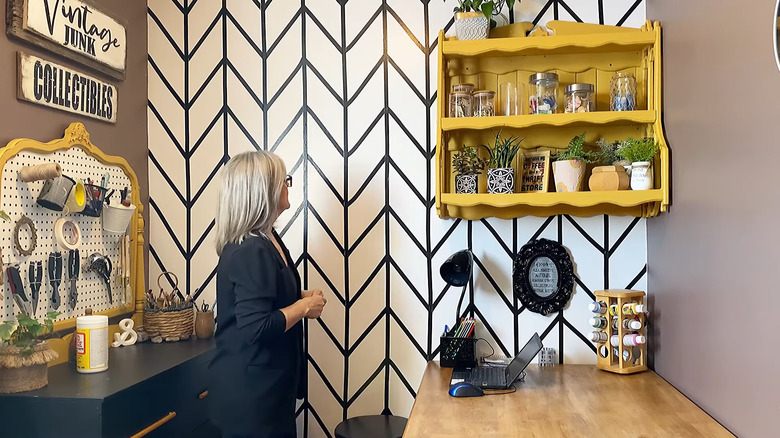 Creator standing in her redesigned space with an electrical tape pattern on a white wall behind her
