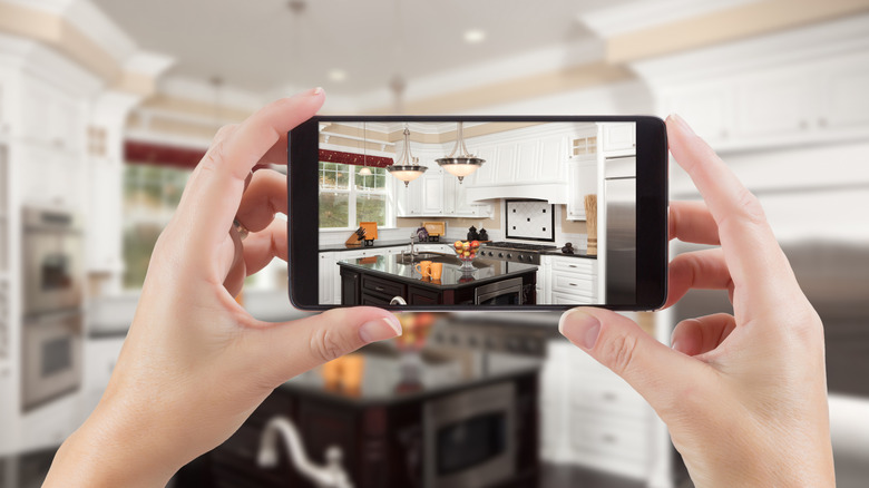 Person holding a smartphone and taking a picture of a kitchen