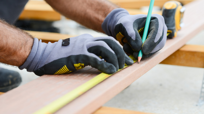 Man marking a wooden board to prepare for cutting it
