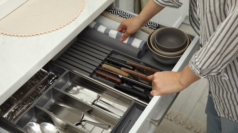 A person stands over an organized kitchen drawer with storage containers and silverware inside