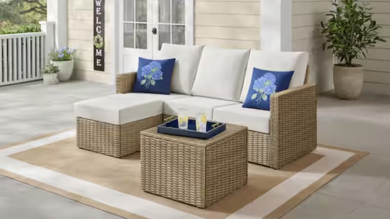 A wicker Hampton Bay outdoor lounger with almond cushions and a side table on a patio