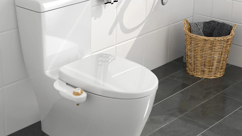 A small bidet attachment peeking out of a white toilet with a closed seat