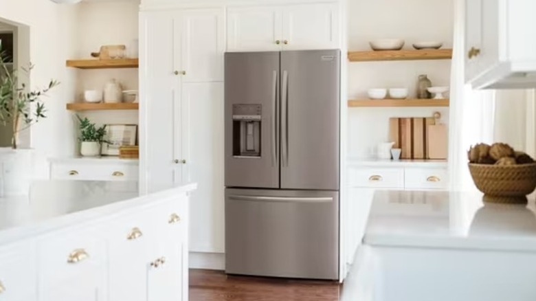 A stainless steel refrigerator in a white kitchen with wood shelves