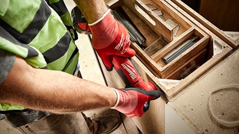 A man holding an oscillating tool in both his hands against a wood surface