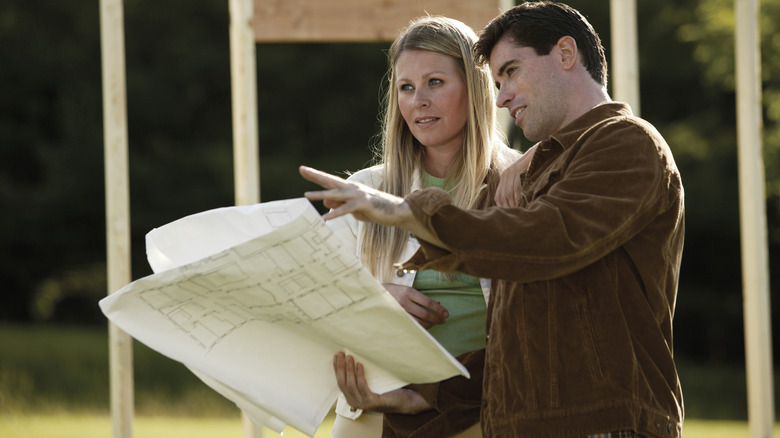 A young couple looks at a site plan while standing near a newly framed house.