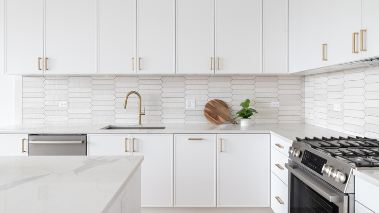 White kitchen with brass cabinets pulls and sink faucet.