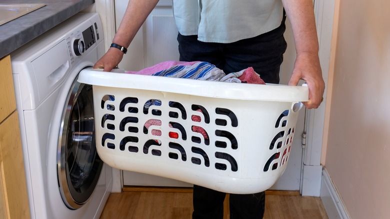 A person holds a laundry basket full of clothes near a front-loading washing machine