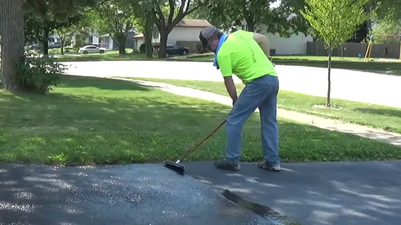 Man resealing asphalt driveway using thin coat of DIY blacktop sealer at home