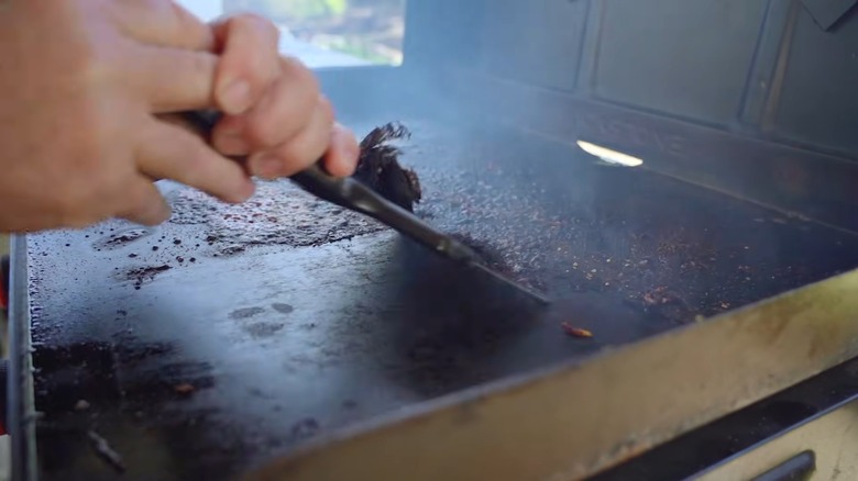 Man using a scraper to remove buildup on his Blackstone griddle