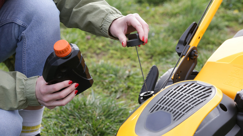 Someone checking the oil on a push lawn mower as part of routine maintenance.