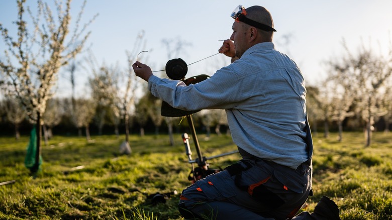 Man in orchard setting restringing a string trimmer