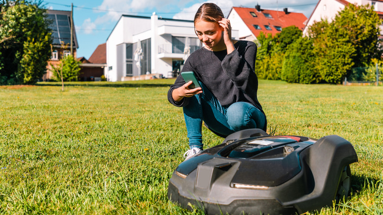 Young woman controlling a robot lawn mower with her smart phone in the summer