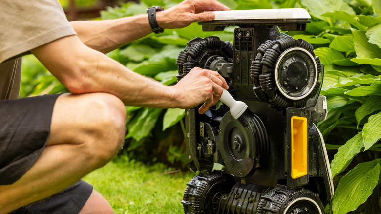 a person cleaning the underside of a robot lawn mower