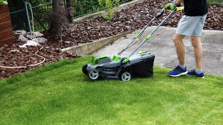 Man using a cordless lawn mower on a sloped surface