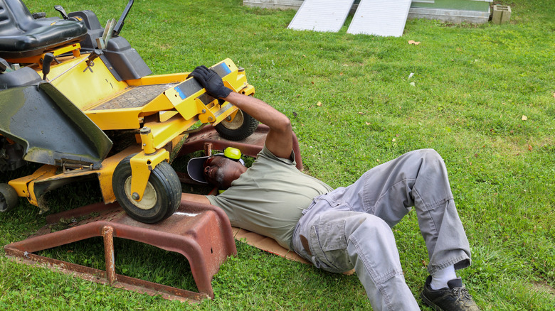 Man looking under the hood of a mower to repair it
