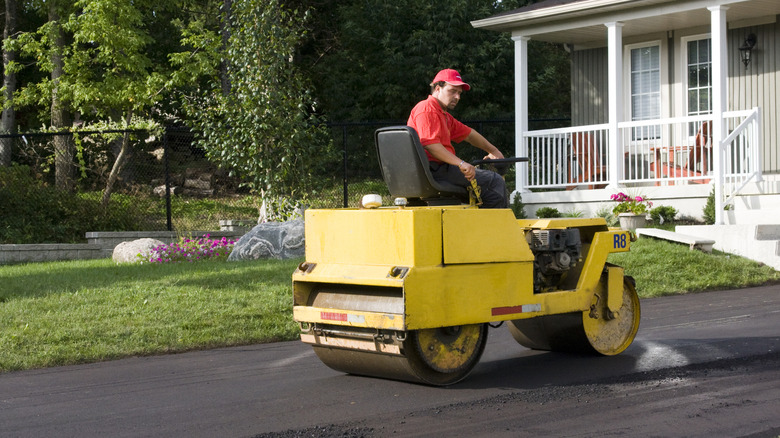 A construction worker finishes a new residential asphalt driveway with a roller