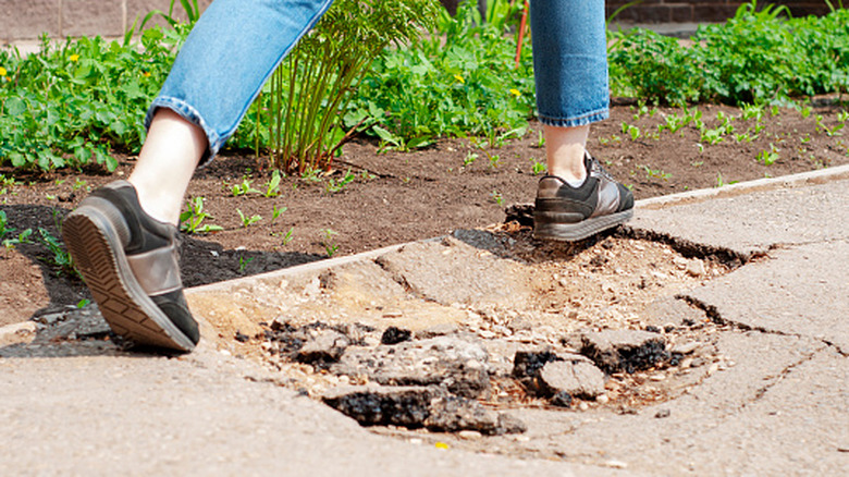 Feet stepping over hole in asphalt