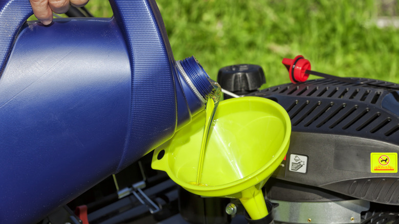 Hand pouring oil in a lawn mower through a funnel