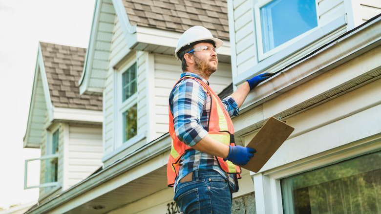 A man wearing an orange safety vest inspects a roof