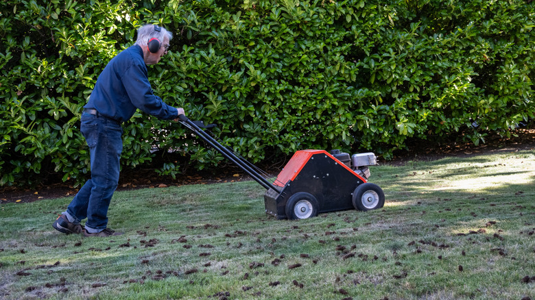 Man pushing a core aerator machine across lawn