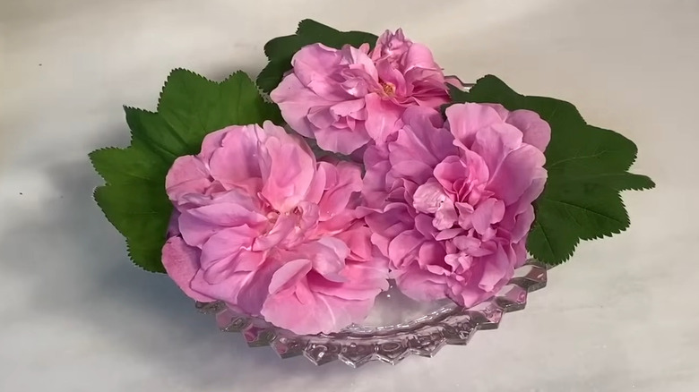 Pink flowers floating in crystal dish set on a table.