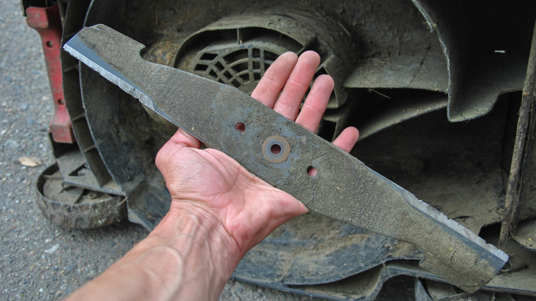 Hand holding a worn lawn mower blade