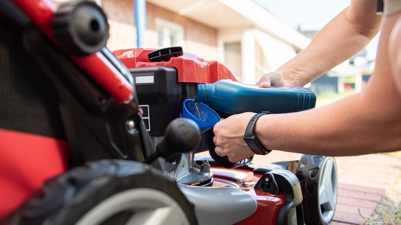 Person pouring new oil into a lawn mower, using a funnel
