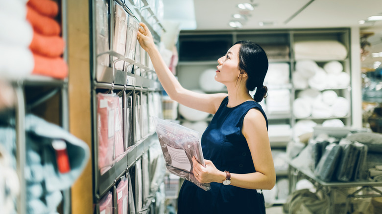 Woman browsing packaged bed sheets in a home goods store