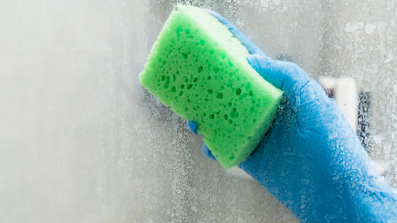 gloved hand with sponge wiping stained shower glass