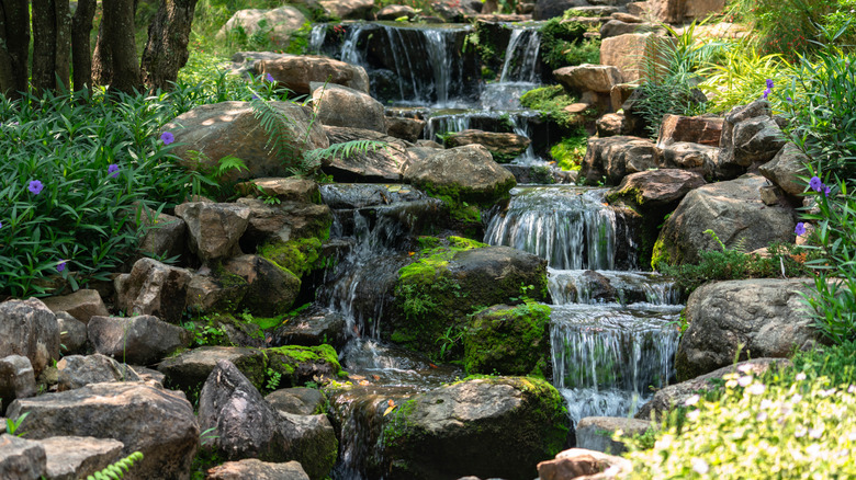A tiered rock waterfall in a garden. You should rely on concrete when adding a water feature to your yard.