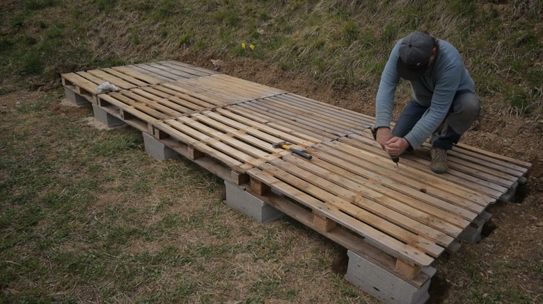Wood pallets set on cinder blocks, with a man on top screwing the pallets together