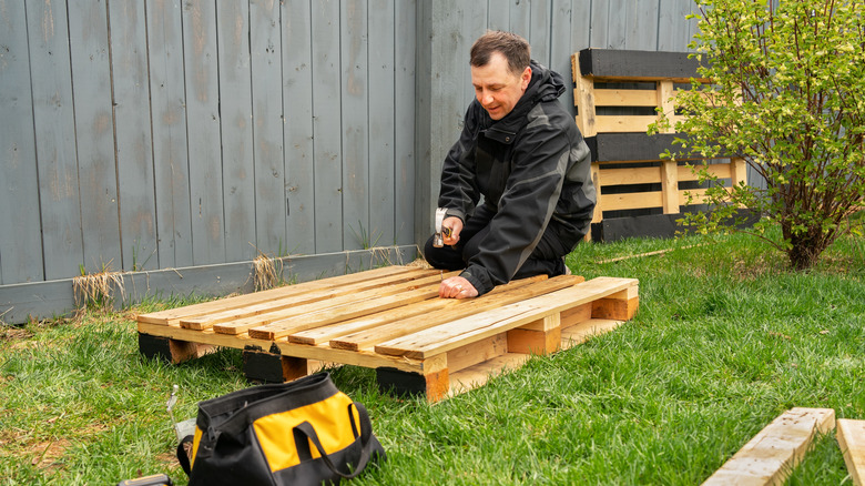 Man on a wood pallet hammering nails into it