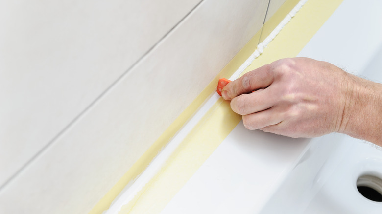 hand smoothing silicone sealant with painters tape to get sharp lines