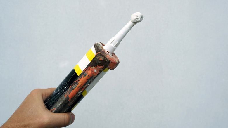person holding caulk gun against a grey wall