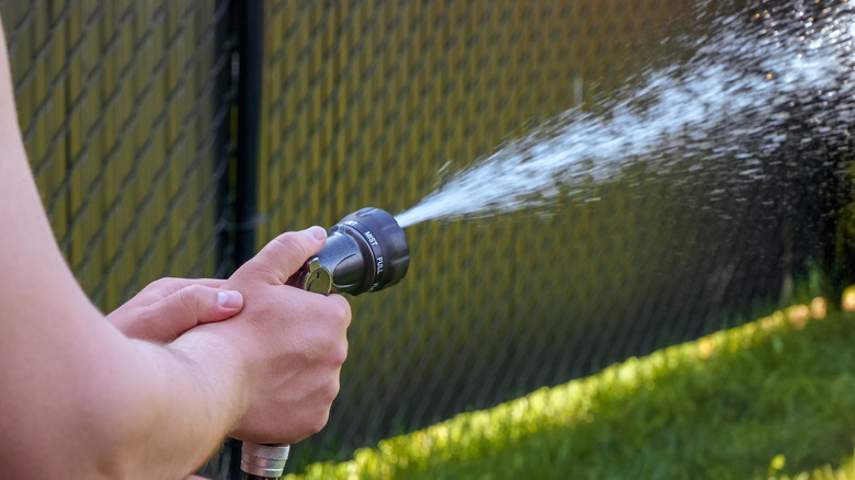 Person adjusting nozzle on garden hose with fence in background