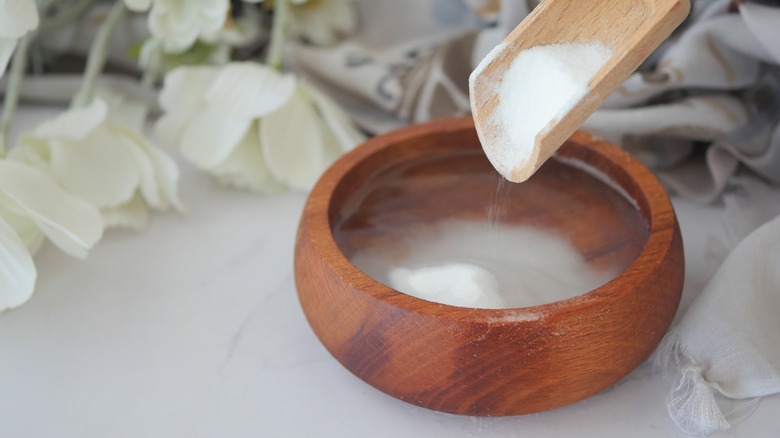 Filling a wooden bowl with baking soda using a wooden scoop