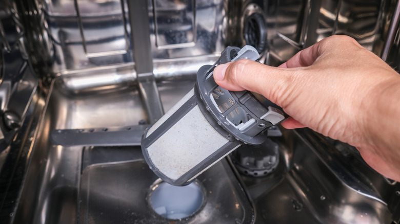 A person pulling out the filter from a dishwasher to clean it with vinegar and water.